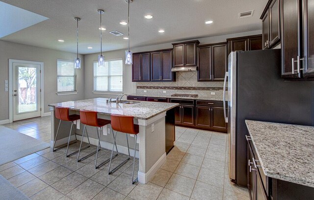 5821 Viejo Dr, Austin, TX 78738 - kitchen featuring light tile patterned flooring, a center island with sink, light stone countertops, tasteful backsplash, and dark brown cabinets