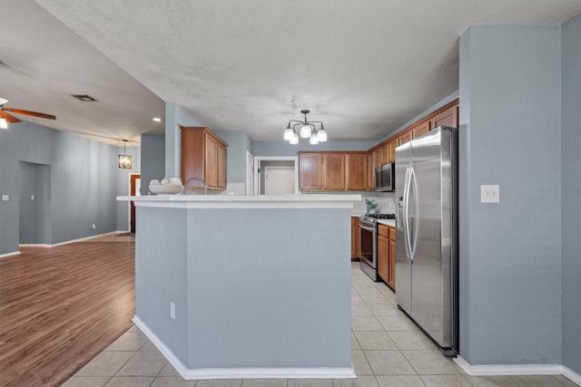 1503 Sherry Dr, Taylor, TX 76574 - kitchen featuring stainless steel appliances, ceiling fan, brown cabinets, a chandelier, and light tile patterned flooring