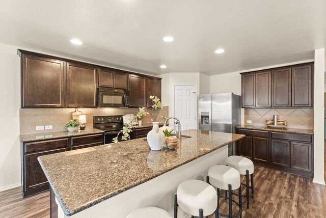 1305 Cozy Creek Dr, Temple, TX 76502 - kitchen featuring black appliances, dark wood-type flooring, dark brown cabinets, decorative backsplash, and a breakfast bar