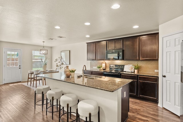 1305 Cozy Creek Dr, Temple, TX 76502 - kitchen with black appliances, dark stone countertops, dark wood-type flooring, a kitchen bar, and backsplash
