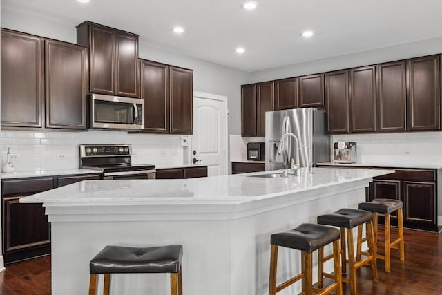 7016 Lickeen Ct, Austin, TX 78744 - kitchen featuring stainless steel appliances, a kitchen breakfast bar, dark wood finished floors, decorative backsplash, and a center island with sink
