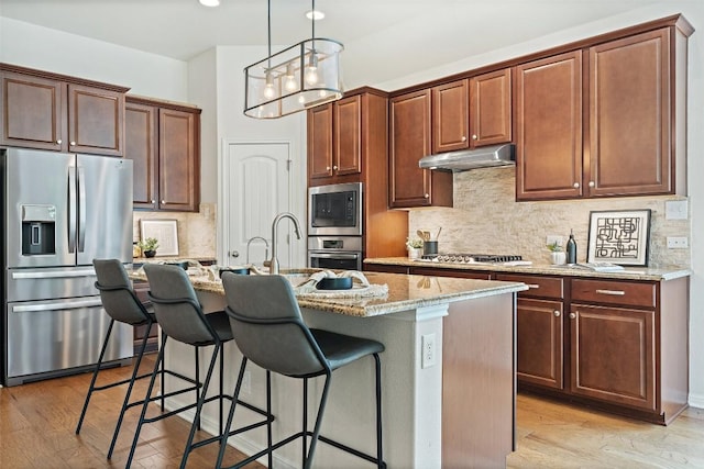 18517 Tanner Bayou Loop, Austin, TX 78738 - kitchen with appliances with stainless steel finishes, under cabinet range hood, a breakfast bar, light stone countertops, and a kitchen island with sink