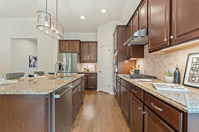 18517 Tanner Bayou Loop, Austin, TX 78738 - kitchen featuring appliances with stainless steel finishes, under cabinet range hood, wood finished floors, light stone countertops, and recessed lighting