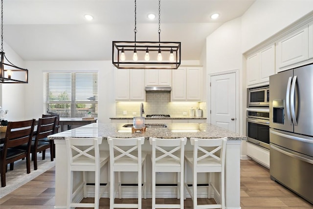 22300 Chipotle Pass, Spicewood, TX 78669 - kitchen with appliances with stainless steel finishes, a chandelier, decorative backsplash, a kitchen island with sink, and light wood-type flooring