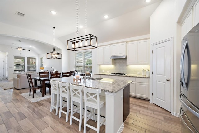 22300 Chipotle Pass, Spicewood, TX 78669 - kitchen featuring vaulted ceiling, appliances with stainless steel finishes, under cabinet range hood, decorative backsplash, and white cabinets
