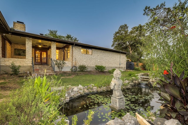 10701 Glass Mountain Trl, Austin, TX 78750 - view of front of house featuring a small pond, stone siding, a chimney, and covered porch