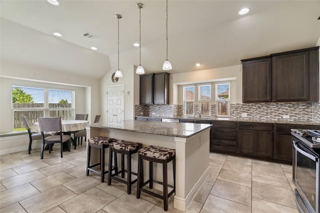 136 W Highfield St, Hutto, TX 78634 - kitchen with stainless steel range with gas stovetop, tasteful backsplash, a kitchen island, dark brown cabinetry, and vaulted ceiling