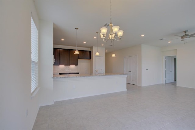 7517 Ballydawn Dr, Austin, TX 78744 - kitchen featuring backsplash, dark brown cabinetry, light stone counters, a chandelier, and pendant lighting