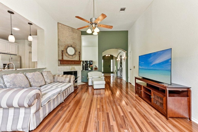 4005 Travis Country Cir, Austin, TX 78735 - living room featuring arched walkways, light wood-type flooring, ceiling fan, a fireplace, and a high ceiling