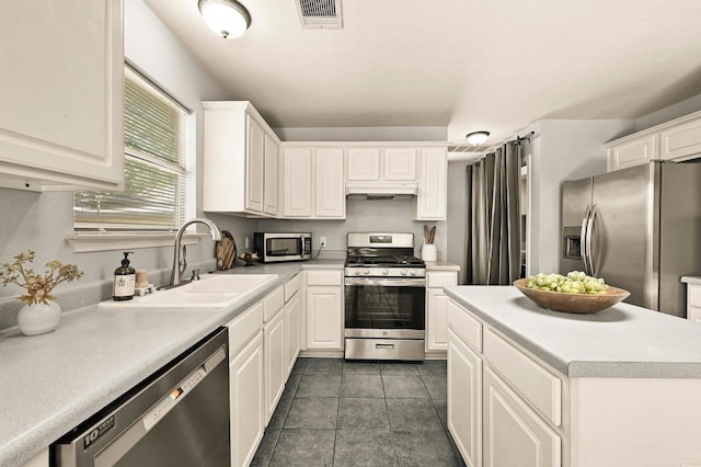 4460 Bremner Dr, Austin, TX 78749 - kitchen with stainless steel appliances, white cabinets, light countertops, under cabinet range hood, and dark tile patterned flooring