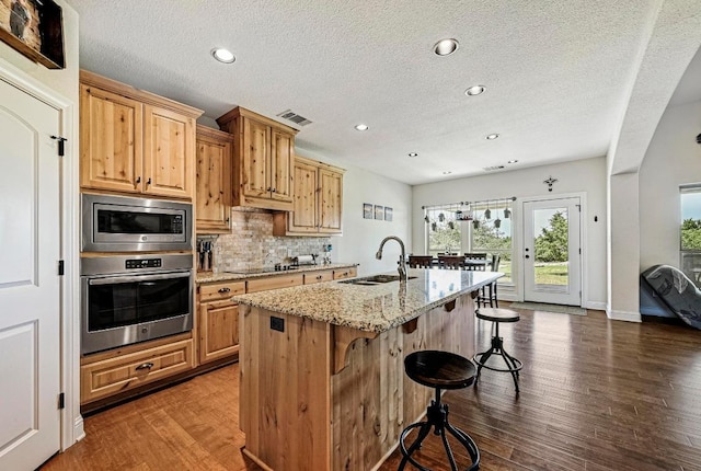312 First Down Dash, Bertram, TX 78611 - kitchen featuring stainless steel appliances, a kitchen breakfast bar, light stone counters, backsplash, and dark wood finished floors