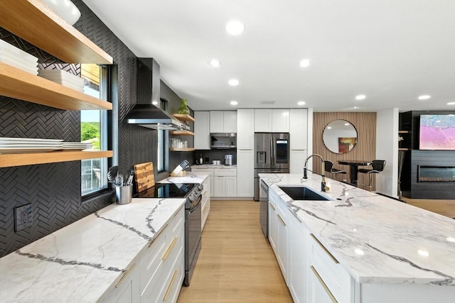 12501 Mixson Dr, Austin, TX 78732 - kitchen featuring open shelves, wall chimney exhaust hood, appliances with stainless steel finishes, white cabinetry, and light wood-style flooring