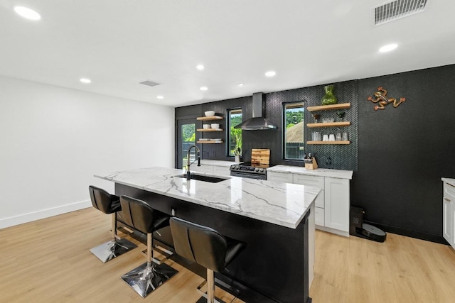 12501 Mixson Dr, Austin, TX 78732 - kitchen featuring wall chimney range hood, open shelves, light wood-type flooring, a breakfast bar, and recessed lighting