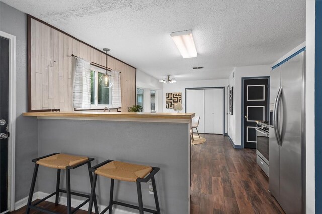 501 Battlecreek Ln, Leander, TX 78641 - kitchen with appliances with stainless steel finishes, a textured ceiling, a breakfast bar, a peninsula, and dark wood-style flooring