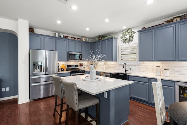 7625 Brecourt Manor Way, Austin, TX 78739 - kitchen featuring appliances with stainless steel finishes, a kitchen island, a breakfast bar area, backsplash, and blue cabinets