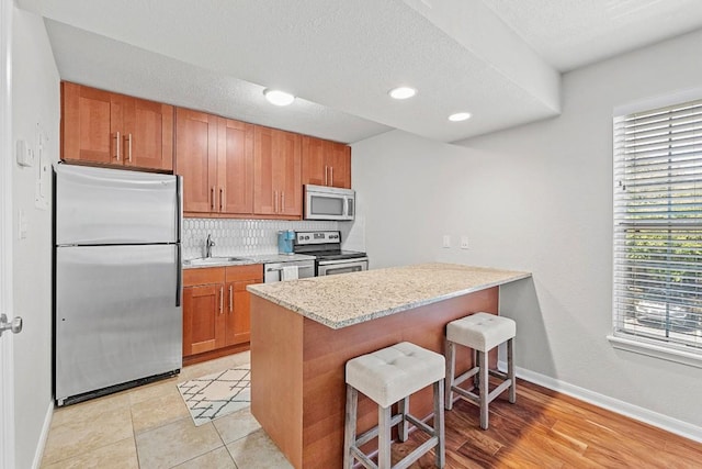 7685 Northcross Dr Unit 720, Austin, TX 78757 - kitchen with appliances with stainless steel finishes, a breakfast bar, brown cabinets, a peninsula, and decorative backsplash
