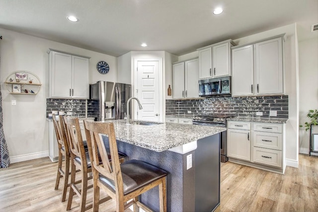 336 Gaida Loop, Georgetown, TX 78628 - kitchen with appliances with stainless steel finishes, light wood-type flooring, a kitchen island with sink, light stone counters, and tasteful backsplash