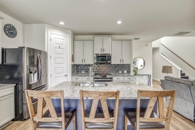 336 Gaida Loop, Georgetown, TX 78628 - kitchen featuring stainless steel appliances, light stone counters, light wood-style floors, decorative backsplash, and a breakfast bar area