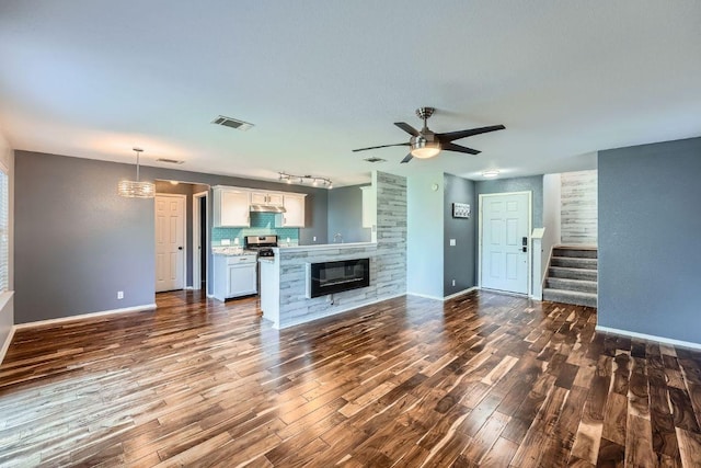 14418 Cummins Way, Manor, TX 78653 - unfurnished living room with dark wood-type flooring, ceiling fan, stairs, track lighting, and a glass covered fireplace