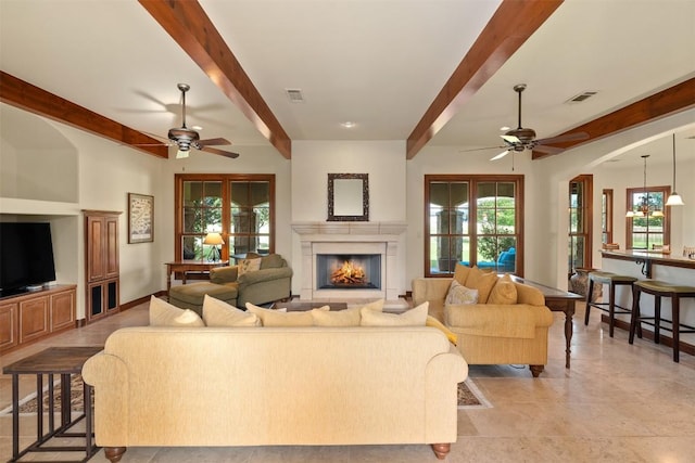 307 Goodnight Dr, Georgetown, TX 78628 - living room with a ceiling fan, beam ceiling, a warm lit fireplace, and arched walkways
