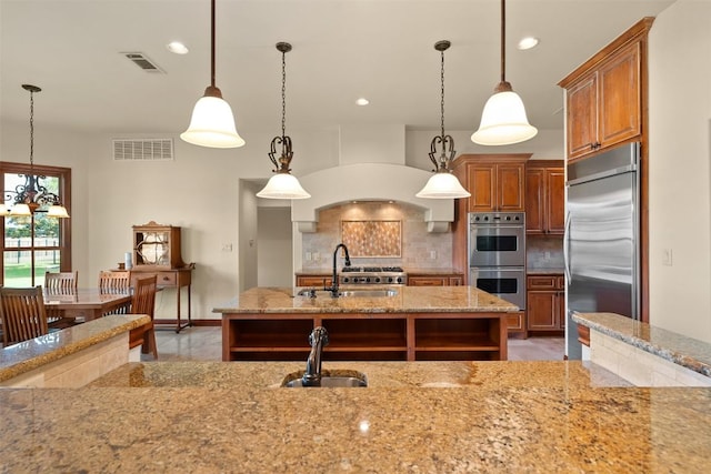 307 Goodnight Dr, Georgetown, TX 78628 - kitchen featuring appliances with stainless steel finishes, brown cabinets, backsplash, light stone countertops, and hanging light fixtures
