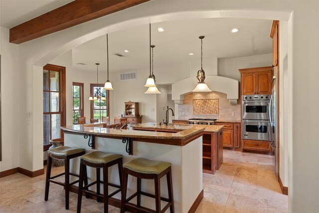 307 Goodnight Dr, Georgetown, TX 78628 - kitchen with stainless steel appliances, a large island, brown cabinets, arched walkways, and backsplash