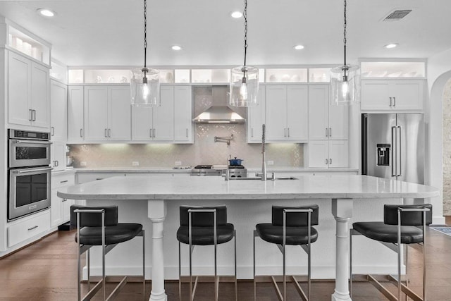 203 Black Stone Cv, Driftwood, TX 78619 - kitchen featuring stainless steel appliances, wall chimney exhaust hood, white cabinets, tasteful backsplash, and a breakfast bar area