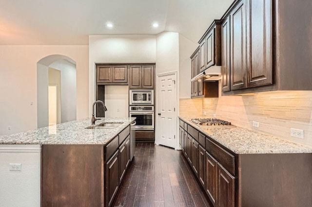 851 Catalina Ln, Austin, TX 78737 - kitchen featuring appliances with stainless steel finishes, backsplash, arched walkways, under cabinet range hood, and a center island with sink