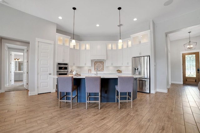 213 Woodland Hills Dr, Georgetown, TX 78633 - kitchen featuring stainless steel appliances, light countertops, light wood finished floors, an island with sink, and decorative backsplash