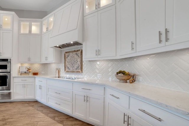 213 Woodland Hills Dr, Georgetown, TX 78633 - kitchen with black electric stovetop, premium range hood, white cabinets, and stainless steel double oven