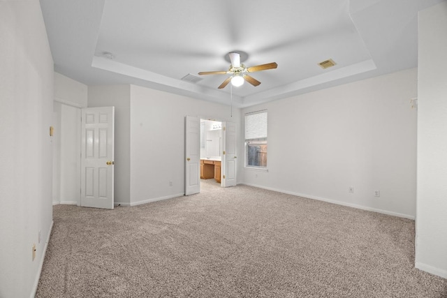 716 Bent Wood Pl, Round Rock, TX 78665 - unfurnished bedroom with a tray ceiling, light carpet, connected bathroom, and ceiling fan