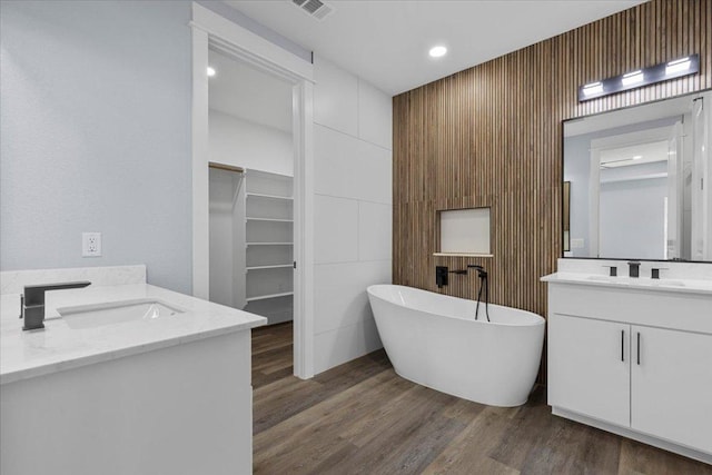 103 W Pauwela Ln, Bastrop, TX 78602 - bathroom featuring two vanities, a soaking tub, wood finished floors, a spacious closet, and recessed lighting