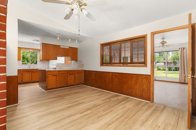 6804 Miranda Dr, Austin, TX 78752 - kitchen with a ceiling fan, brown cabinetry, light wood-type flooring, a textured ceiling, and a wainscoted wall