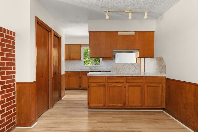 6804 Miranda Dr, Austin, TX 78752 - kitchen featuring brown cabinets, light countertops, light wood finished floors, decorative backsplash, and wainscoting