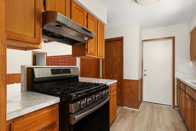 6804 Miranda Dr, Austin, TX 78752 - kitchen featuring stainless steel gas stove, under cabinet range hood, light wood-type flooring, brown cabinets, and a textured ceiling