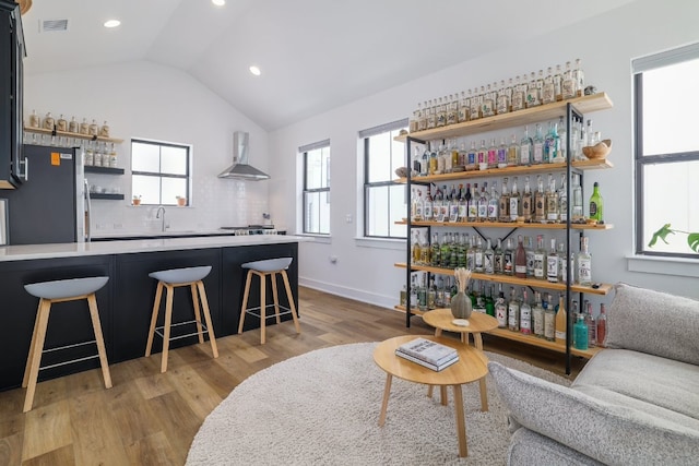 3108 Chennault St, Austin, TX 78723 - indoor wet bar with freestanding refrigerator, wall chimney range hood, light wood-style flooring, vaulted ceiling, and decorative backsplash