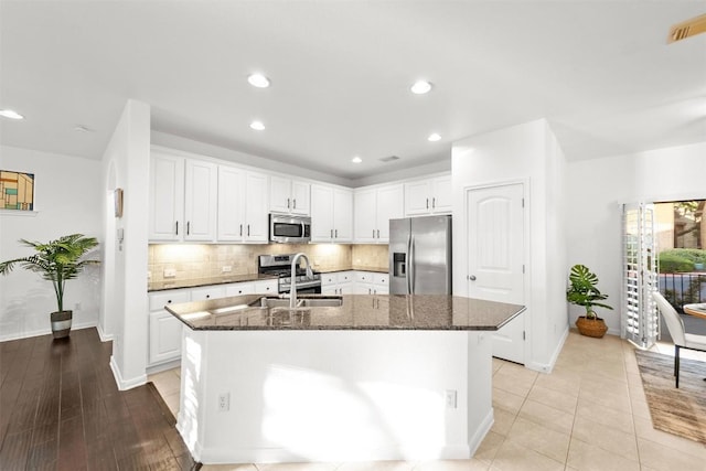11400 W Parmer Ln Unit 44, Cedar Park, TX 78613 - kitchen featuring appliances with stainless steel finishes, a kitchen island with sink, decorative backsplash, white cabinetry, and dark stone countertops