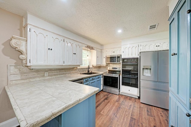 2505 Linwood Rd, Temple, TX 76502 - kitchen with appliances with stainless steel finishes, a textured ceiling, wood finished floors, white cabinets, and a peninsula