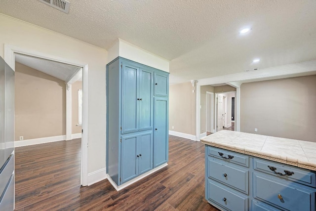 2505 Linwood Rd, Temple, TX 76502 - kitchen featuring blue cabinetry, dark wood-style flooring, ornate columns, tile counters, and a textured ceiling