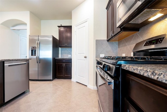 13903 Cantata Ln, Austin, TX 78660 - kitchen with stainless steel appliances, dark brown cabinetry, backsplash, dark stone countertops, and light tile patterned floors