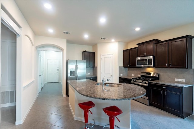 13903 Cantata Ln, Austin, TX 78660 - kitchen featuring appliances with stainless steel finishes, light tile patterned floors, decorative backsplash, dark stone counters, and dark brown cabinets
