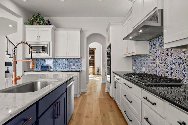 4509 Port Bari Dr, Leander, TX 78641 - kitchen featuring blue cabinetry, stainless steel appliances, exhaust hood, white cabinets, and arched walkways