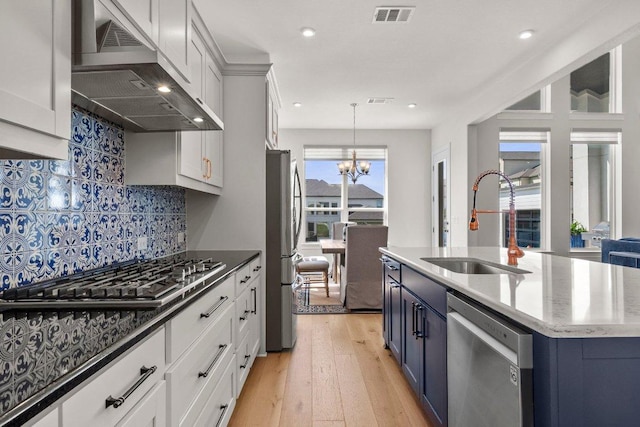 4509 Port Bari Dr, Leander, TX 78641 - kitchen featuring stainless steel appliances, range hood, a chandelier, light wood-style floors, and backsplash