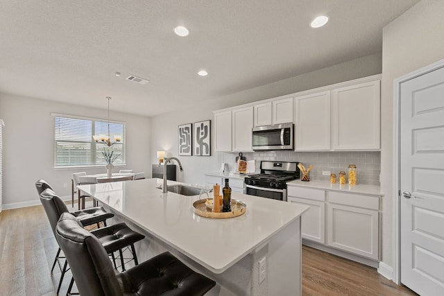 16941 Aventura Ave, Pflugerville, TX 78660 - kitchen featuring appliances with stainless steel finishes, tasteful backsplash, an island with sink, a kitchen bar, and white cabinetry