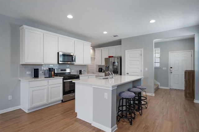12003 Curlin Cv, Buda, TX 78610 - kitchen with stainless steel appliances, tasteful backsplash, a breakfast bar area, a center island with sink, and white cabinetry
