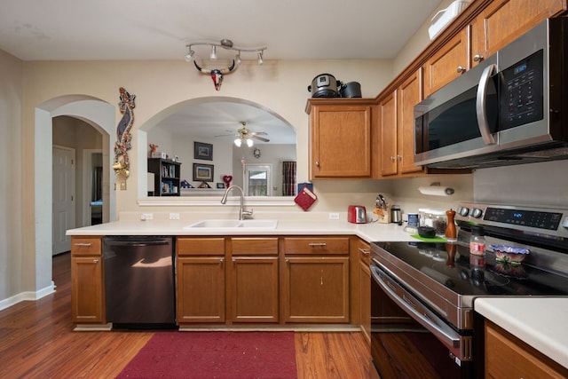 18112 Skysail Dr, Manor, TX 78653 - kitchen with appliances with stainless steel finishes, wood finished floors, brown cabinetry, light countertops, and arched walkways