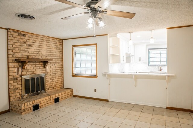 215 Edward Ln, Brenham, TX 77833 - unfurnished living room featuring a textured ceiling, ornamental molding, a brick fireplace, a ceiling fan, and light tile patterned floors