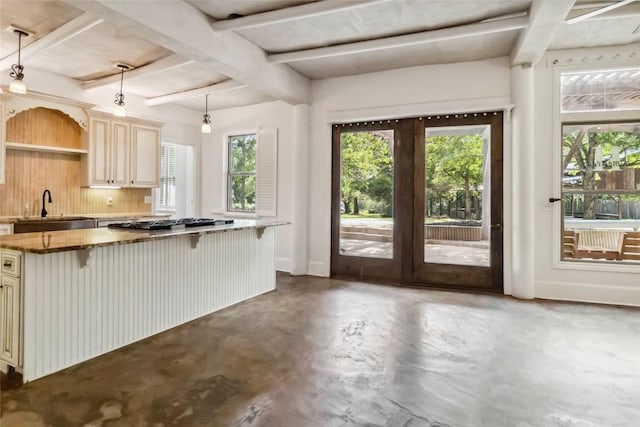 208 Old Potato Rd, Paige, TX 78659 - kitchen with cream cabinets, concrete flooring, stainless steel gas stovetop, a breakfast bar, and beam ceiling