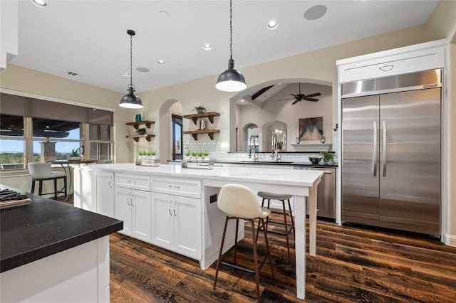 3810 Pawnee Pass, Austin, TX 78738 - kitchen with appliances with stainless steel finishes, arched walkways, dark wood-style flooring, white cabinetry, and backsplash