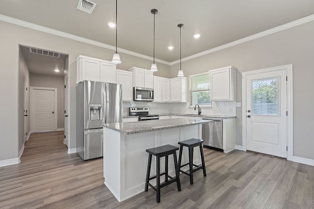 103 W Tomlinson St, Florence, TX 76527 - kitchen featuring stainless steel appliances, a kitchen island, wood finished floors, white cabinets, and tasteful backsplash